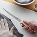 A person holding a Dexter-Russell Sani-Safe narrow fillet knife over a fish on a cutting board.