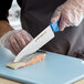 A person in a plastic glove cutting a piece of fish with a Dexter-Russell blue chef knife.