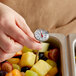 A person's hand using a Taylor pocket probe thermometer to check the temperature of fruit salad.