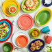 A group of green, yellow, and orange Acopa Capri stoneware plates and bowls on a table with a grapefruit slice on a green plate.