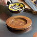 A person using a Valor Rustic Chestnut round rubberwood underliner to hold a pan of food over a wooden plate.