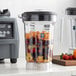A Waring blender full of fruit sits on a counter. The blender has a grey blender jar with a lid.