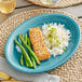 An Acopa Caribbean turquoise stoneware coupe platter with asparagus, rice, and salmon on a table.