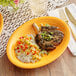 An Acopa mango orange oval stoneware coupe platter with food on a table.