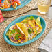 A group of tacos on a Caribbean turquoise Acopa oval platter.