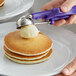 A person using a purple Thunder Group ice cream scoop to put butter on pancakes.