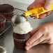 A hand using a yellow Thunder Group EZ Grip Disher to scoop ice cream onto a chocolate cupcake.