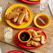 A table set with Acopa Capri mango orange stoneware bouillon bowls and plates of fried spring rolls and dumplings.