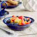 A deep sea cobalt Acopa stoneware bowl filled with fruit on a table.