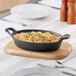 A black Valor mini cast iron casserole dish filled with macaroni and cheese on a wooden surface.