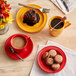 A table with red Acopa Capri stoneware mugs filled with coffee on a table with plates of food.