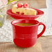 An Acopa Capri passion fruit red stoneware cup filled with a drink on a table with a slice of cheesecake.