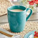 An Acopa Capri Caribbean turquoise stoneware mug filled with a white drink on a table with a plate of food.