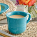 A close-up of a Caribbean turquoise Acopa Capri stoneware cup filled with a drink on a table with a place mat.