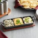 A Valor pre-seasoned cast iron tray with three compartments of dips and chips on a table.
