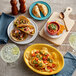 A table with Acopa Capri coral stoneware bouillon bowls of soup and plates of tacos and chips.