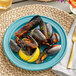A plate of mussels with lemon and a fork on an Acopa Caribbean turquoise stoneware plate.