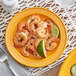 An Acopa Capri mango orange stoneware plate with shrimp and lime on a table.