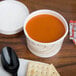 A Solo Symphony paper soup cup filled with soup on a table with crackers.