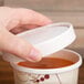 A hand holding a Solo Symphony paper cup of soup with a lid.