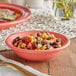 An Acopa Capri coral stoneware fruit bowl filled with food on a table.