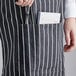 A person holding a pen in the pocket of a black and white striped Choice Bistro Apron.