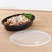 A Pactiv Newspring black plastic oval container of pasta with cheese and parsley on a wooden table.