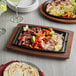 A Valor cast iron fajita skillet with food on a wood surface.