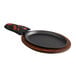 A Valor oval cast iron fajita skillet with a wooden handle on a wooden table.