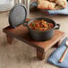 A Valor mini cast iron pot of soup with meat and vegetables sits on a rustic wooden stand.