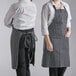 Two women wearing black and white striped Choice bib aprons in a professional kitchen.