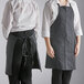 A man and a woman wearing Choice black and white pinstripe bib aprons in a professional kitchen.