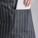 A person's hand putting a piece of paper in a pocket on a Choice Black and White Pinstripe Poly-Cotton Bib Apron.