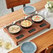 A Valor rustic chestnut display stand with 3 cast iron bowls of food on a table.