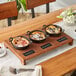 A rustic wood display stand with three cast iron dishes of food on a wood table.