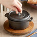 A hand holds a Valor pre-seasoned cast iron pot with a chestnut finish on a wooden table.