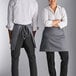 A man and woman wearing grey Choice half bistro aprons standing next to each other on a counter.