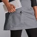 A person wearing a gray Choice half bistro apron with 2 pockets holding a paper and a pen.