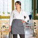 A woman in a white shirt and gray Choice half bistro apron standing in a restaurant.