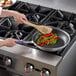 A person cooking vegetables in a Vollrath Wear-Ever non-stick fry pan.