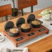 A rustic wooden board with Valor mini cast iron pots filled with food.
