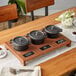 A rustic wooden display stand with 3 black cast iron pots on a table.