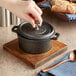 A person's hand pressing a lid on a Valor mini cast iron pot on a table.