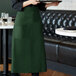 A woman wearing a Choice Hunter Green Bistro Apron holding a tray.