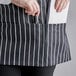A person's hand holding a pen and a piece of paper in a Choice black and white chalk stripe bib apron pocket.