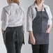 Two women wearing black and white pinstripe bib aprons in a professional kitchen.