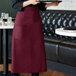 A woman in a black shirt and a burgundy Choice bistro apron holding a plate on a counter.