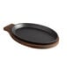 A black oval cast iron fajita skillet on a wooden tray.