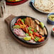 A pan of food with meat and vegetables, sauces, and tortillas on a table with an oak underliner.