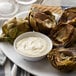 Artichokes on a plate with a white bowl of garlic aioli dip.